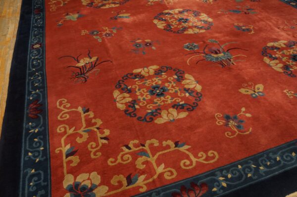 Rust-red rug with yellow and blue floral medallions, a dark navy border, resting on wood plank flooring.