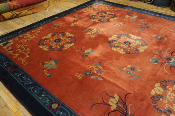 Terracotta rug with gold and blue floral designs and a navy border rests on worn wood plank flooring.