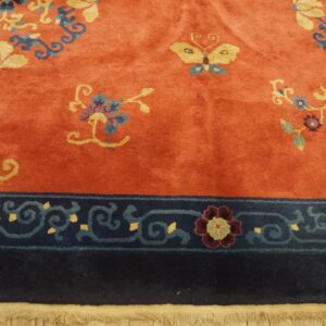 Rust rug with a medium pile featuring yellow and blue floral and butterfly motifs and a dark navy blue border.