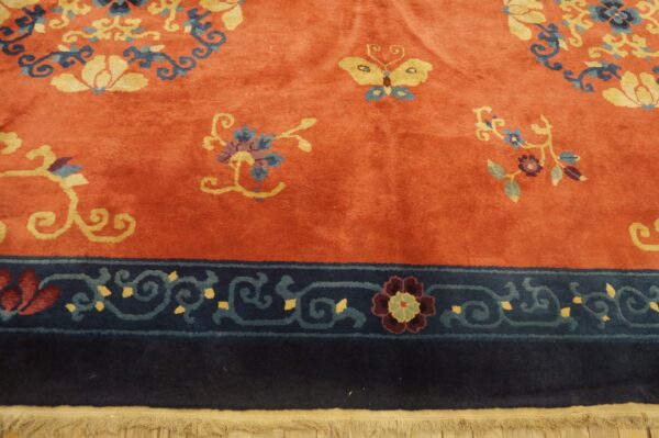 Rust rug with a medium pile featuring yellow and blue floral and butterfly motifs and a dark navy blue border.