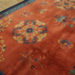 Medium pile coral rug with scattered blue, yellow, and navy floral motifs, shown on light wood planks.
