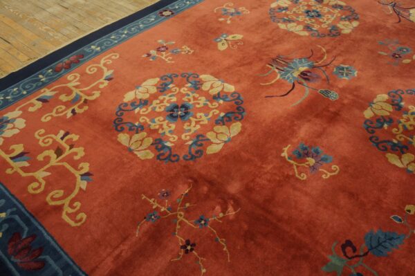 Medium pile coral rug with scattered blue, yellow, and navy floral motifs, shown on light wood planks.