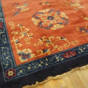 Coral floral rug with a navy blue border rests on light plank hardwood flooring.
