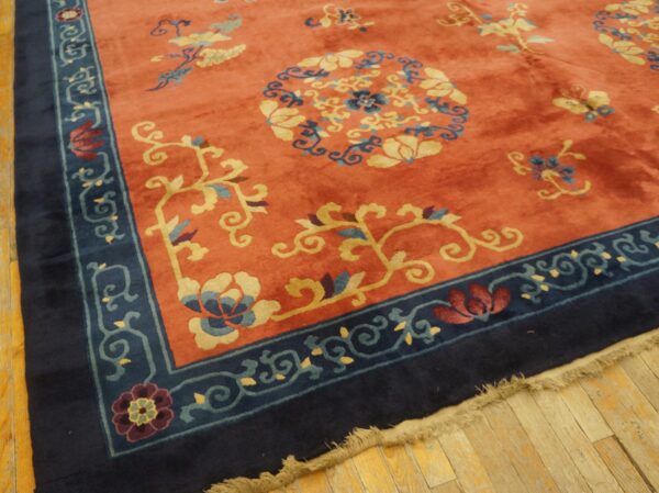 Coral floral rug with a navy blue border rests on light plank hardwood flooring.
