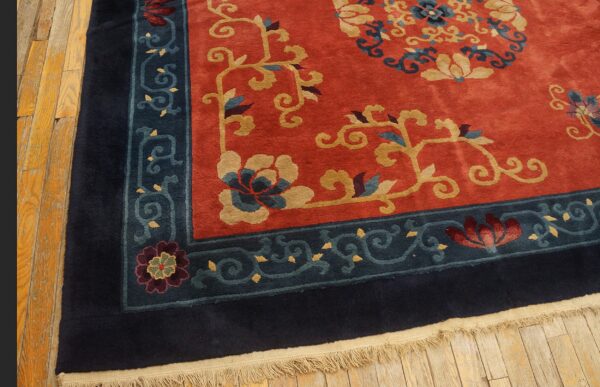 Rust-colored rug with gold floral designs and wide navy blue and teal borders rests on hardwood flooring.