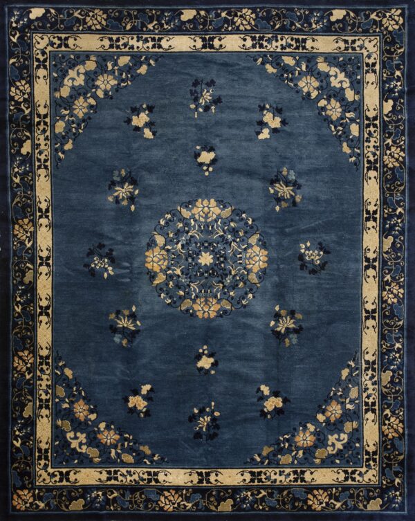 Low-pile indigo rug features gold floral sprays, a central medallion, and wide patterned borders in beige and navy.
