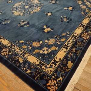 Deep blue floral rug with gold and navy borders and fringe rests on light wood plank flooring.