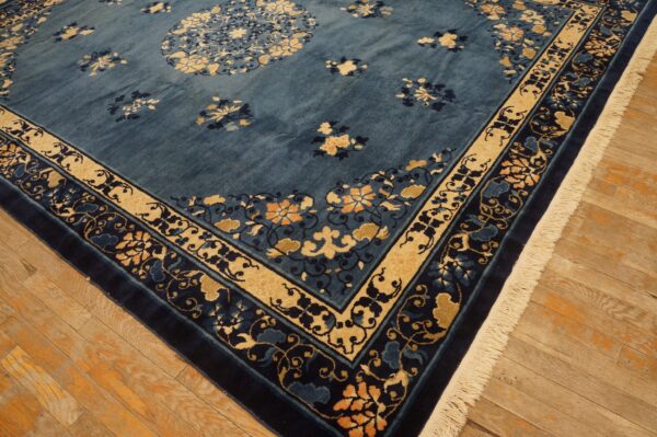 Deep blue floral rug with gold and navy borders and fringe rests on light wood plank flooring.
