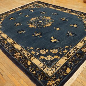 Square deep blue rug with gold floral designs and thick borders on rustic wooden floorboards.