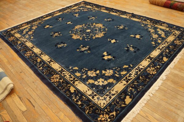 Square deep blue rug with gold floral designs and thick borders on rustic wooden floorboards.