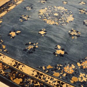 A blue rug featuring a large central medallion and tan border with intricate floral designs on hardwood flooring.