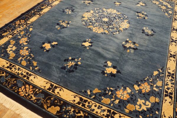 A blue rug featuring a large central medallion and tan border with intricate floral designs on hardwood flooring.