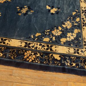 Navy blue rug with intricate gold and dark floral borders resting on light brown hardwood flooring.