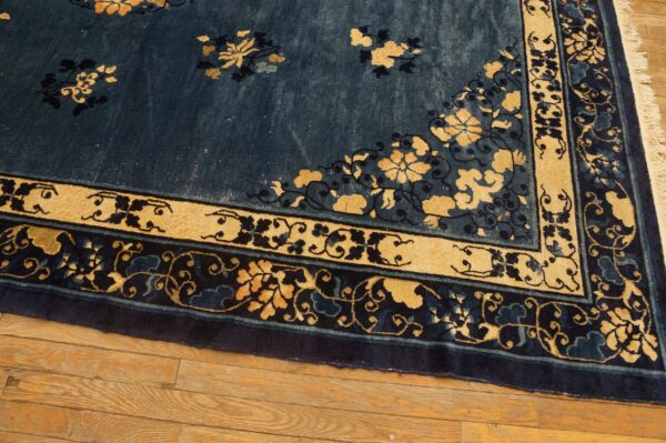 Navy blue rug with intricate gold and dark floral borders resting on light brown hardwood flooring.