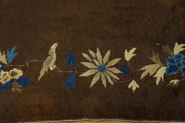 Dark brown rug detail showing a blue, beige, and gray bird and floral border design.