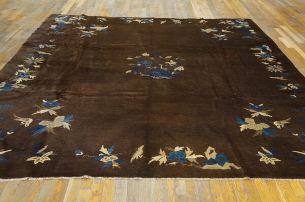 Espresso rug with blue and tan floral and bird motifs covers a bright wooden plank floor.