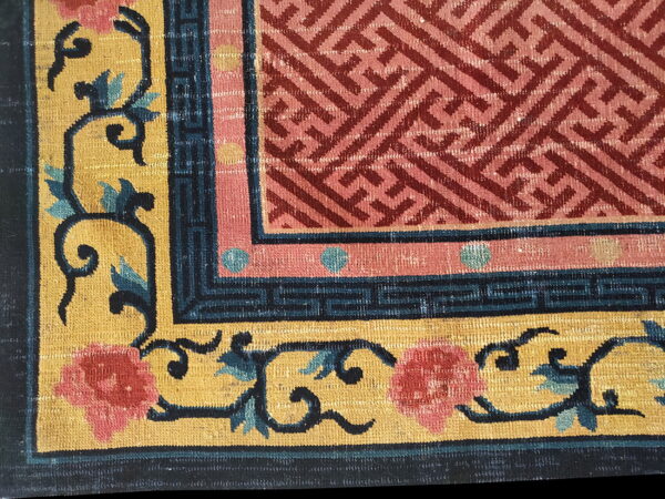 Close-up shows a rug corner with a pink geometric center, dark blue key border, and a gold field with pink and teal florals.