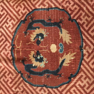 Red rug detail featuring a dark blue twin-dragon medallion surrounded by a tan geometric meander pattern.
