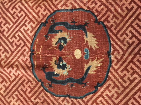 Red rug detail featuring a dark blue twin-dragon medallion surrounded by a tan geometric meander pattern.