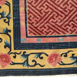 This rug features a maroon geometric center bordered by scrolling vines, pink florals, and yellow ground.