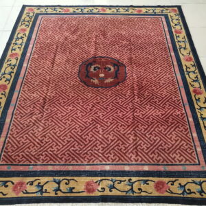 Red geometric rug with a central medallion and ornate gold, blue, and pink floral borders on white tile.
