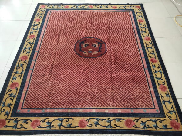 Red geometric rug with a central medallion and ornate gold, blue, and pink floral borders on white tile.