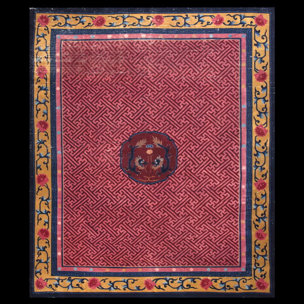 A pink rug features a repeating fret pattern, a central maroon medallion, and a yellow floral border.