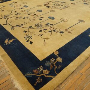A tan rug with navy blue borders and stylized floral branch patterns covers distressed wooden floorboards.
