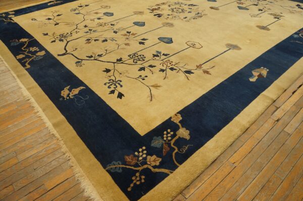 A tan rug with navy blue borders and stylized floral branch patterns covers distressed wooden floorboards.