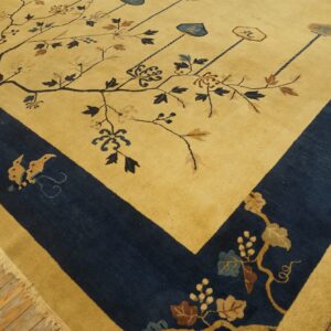 Close-up of a golden yellow rug with a navy blue border, patterned with stylized branches, resting on wood floors.