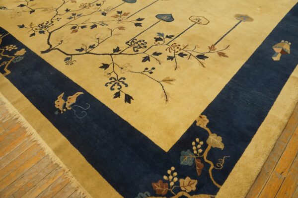 Close-up of a golden yellow rug with a navy blue border, patterned with stylized branches, resting on wood floors.