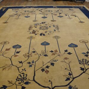 Pale gold rug with a navy blue border and an intricate blue and brown botanical pattern on wood floors.