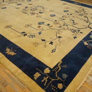 Gold and navy floral rug with vine patterns, detailed motifs, and fringed edge on wood planks.