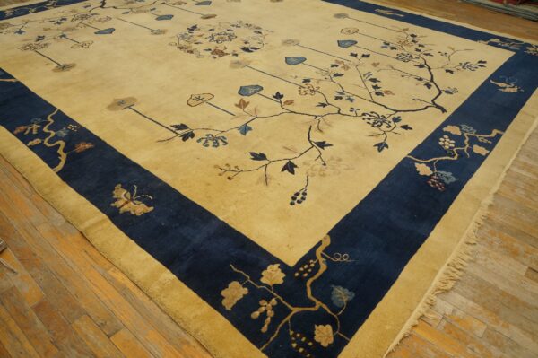 Gold and navy floral rug with vine patterns, detailed motifs, and fringed edge on wood planks.