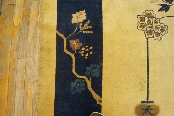 Low-pile yellow rug displaying floral motifs against a navy blue vertical stripe on wood planks.