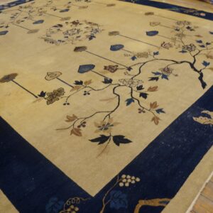 Beige rug with a dark blue border and sprawling botanical pattern rests on light wood plank flooring.