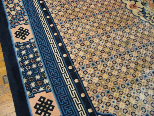 Detailed view of a peach and blue patterned rug with geometric borders lying on wood floors.