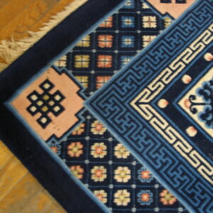 Plush rug detail showing navy, blue, and pink geometric patterns and knot motifs on a wood floor.