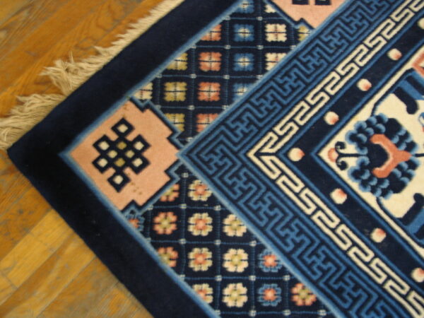 Plush rug detail showing navy, blue, and pink geometric patterns and knot motifs on a wood floor.