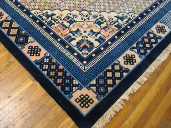 Navy and blue patterned rug corner featuring geometric borders and knots rests on warm-toned wood floorboards.