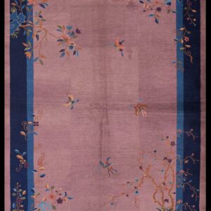 Mauve rug featuring colorful floral vines and dark blue borders lies on worn orange wood flooring.