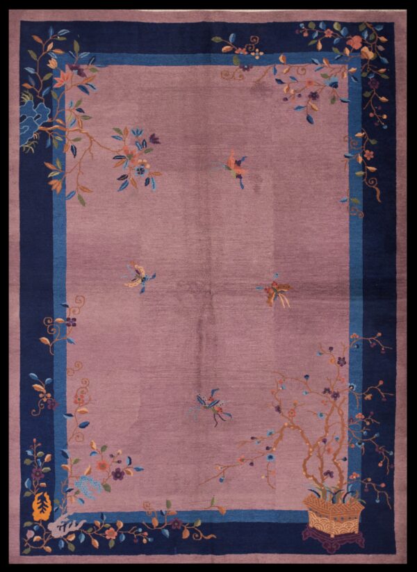Mauve rug featuring colorful floral vines and dark blue borders lies on worn orange wood flooring.