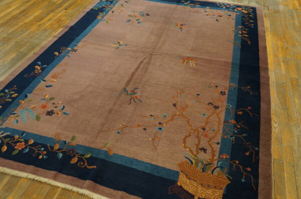 Mauve low-pile rug with colorful floral and bird patterns bordered by navy and teal on wood planks.
