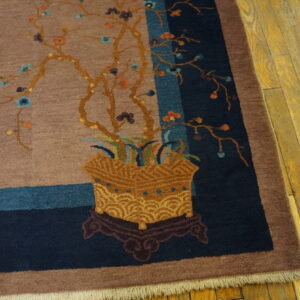Close-up of a taupe rug featuring a potted floral design with blue and navy striped borders on wood floor.