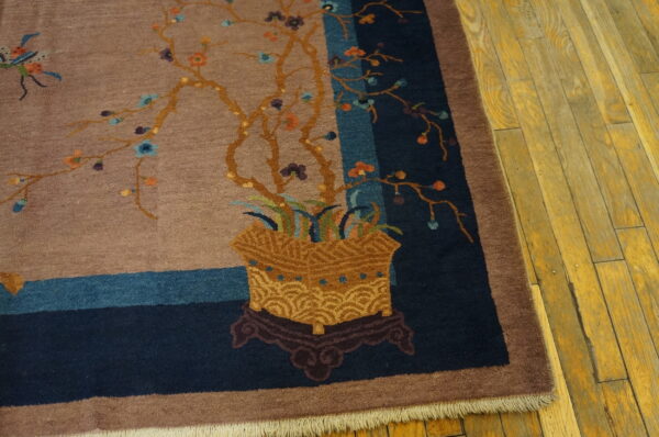 Close-up of a taupe rug featuring a potted floral design with blue and navy striped borders on wood floor.