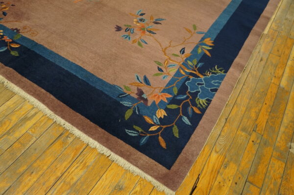 Close-up of a rosy brown rug with navy and blue borders and multicolored floral vine patterns on wood floors.