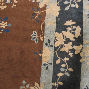 The rug features a rust brown field with cream and blue floral vines, contrasting a dark navy and speckled gray border.