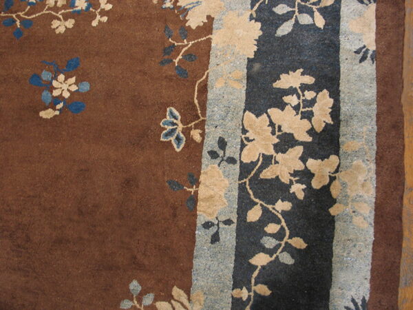 The rug features a rust brown field with cream and blue floral vines, contrasting a dark navy and speckled gray border.