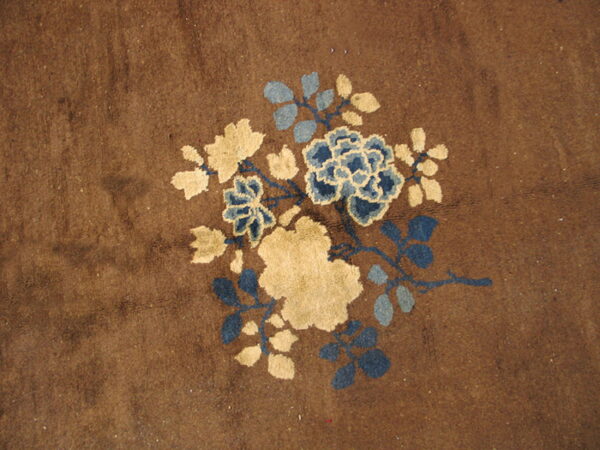 Brown rug featuring a central floral pattern in cream, navy blue, and light blue-gray.