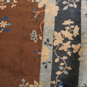 Brown rug with tan and blue floral designs and a wide striped border of gray and dark gray.